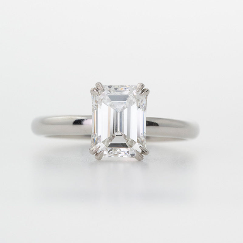 Classic Platinum engagement ring featuring an Emerald cut diamond set with double tiger claw prongs.